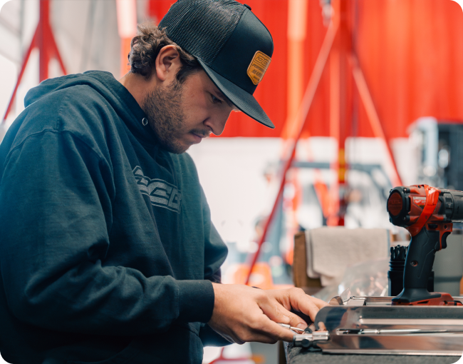Man working on marine equipment in workshop, focused on precision assembly, with tools and a red backdrop, representing DCB Performance Marine's craftsmanship.