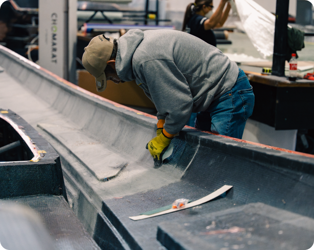 Worker crafting a high-performance marine vessel at DCB Performance Marine, focusing on precision detailing and construction in a workshop setting.