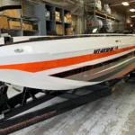 Custom high-performance boat by DCB Performance Marine, showcasing sleek design with white and orange accents, displayed in a workshop setting.
