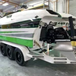 Custom high-performance boat with sleek green and white design, showcasing engineering and luxury, in a workshop setting.