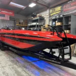 Custom high-performance boat in red and black, showcasing DCB's craftsmanship and design, set in a workshop environment with marine equipment in the background.