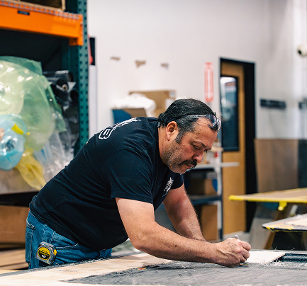 Man working diligently in a workshop, sketching designs on a notepad, surrounded by materials and tools, emphasizing craftsmanship in boat manufacturing at DCB Performance Marine.