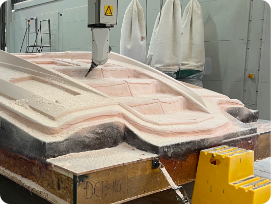 Composite boat hull mold being shaped by CNC machine in DCB Performance Marine's manufacturing facility, showcasing precision engineering and craftsmanship in custom boat production.