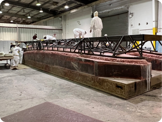Workers in protective gear assembling a composite boat hull with structural bulkheads in a manufacturing facility, showcasing the meticulous build process of DCB Performance Marine's custom vessels.