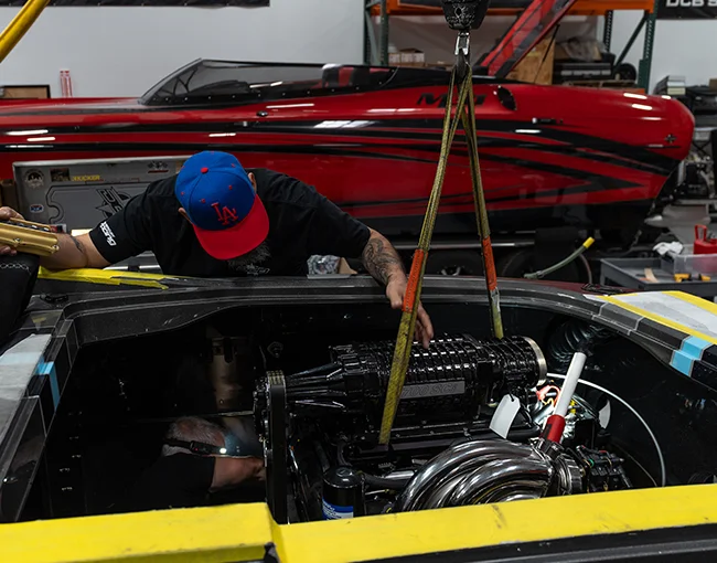 Mechanic inspecting the engine compartment of a high-performance DCB catamaran, featuring a powerful motor and sleek design elements, with a red DCB boat in the background, emphasizing the brand's engineering excellence and craftsmanship.