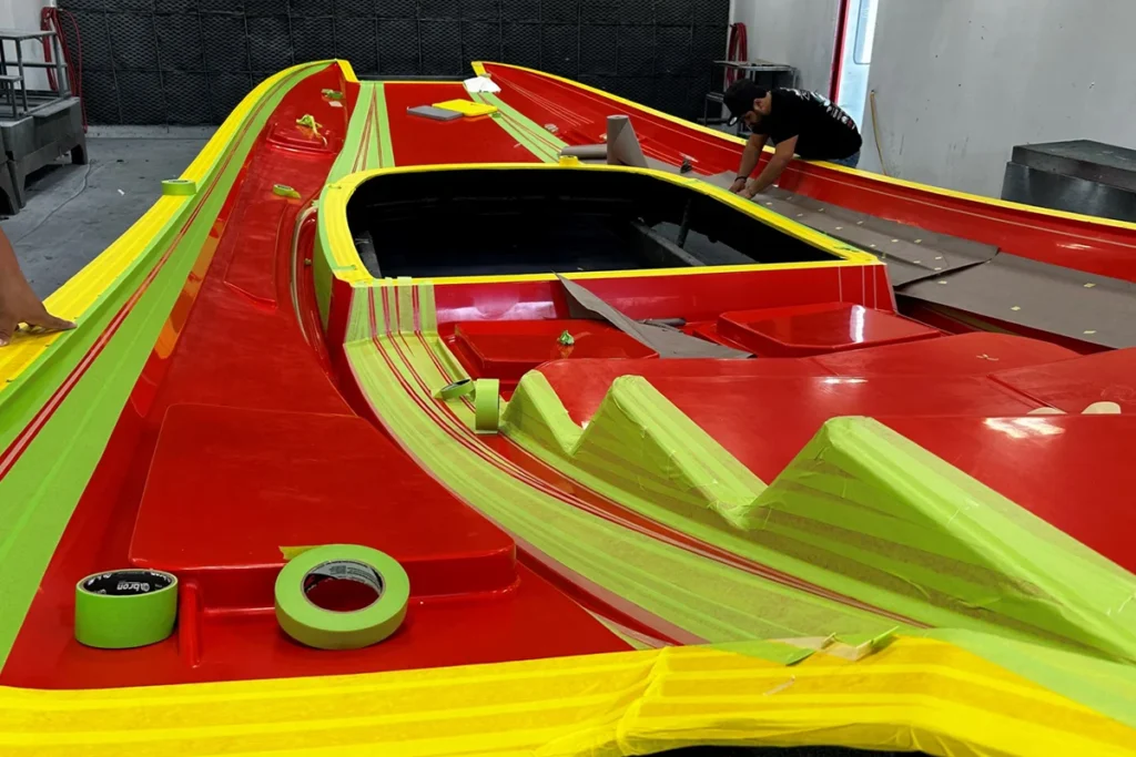 DCB boat mold preparation with red and yellow gelcoat application, featuring masking tape and team member working on details.
