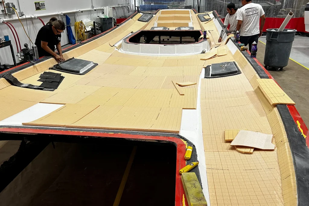 Workers applying masking materials on a boat hull in a manufacturing facility, preparing for gelcoat application in the custom boat building process at DCB Performance Marine.