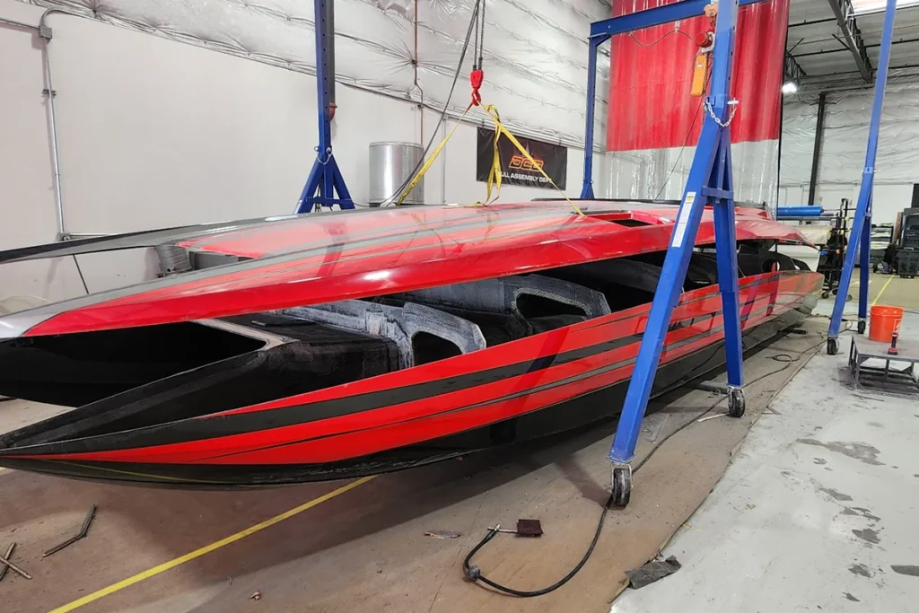 High-performance DCB boat under construction, showcasing composite hull with red and black design, suspended by overhead cranes in a manufacturing facility, highlighting advanced boat-building techniques.