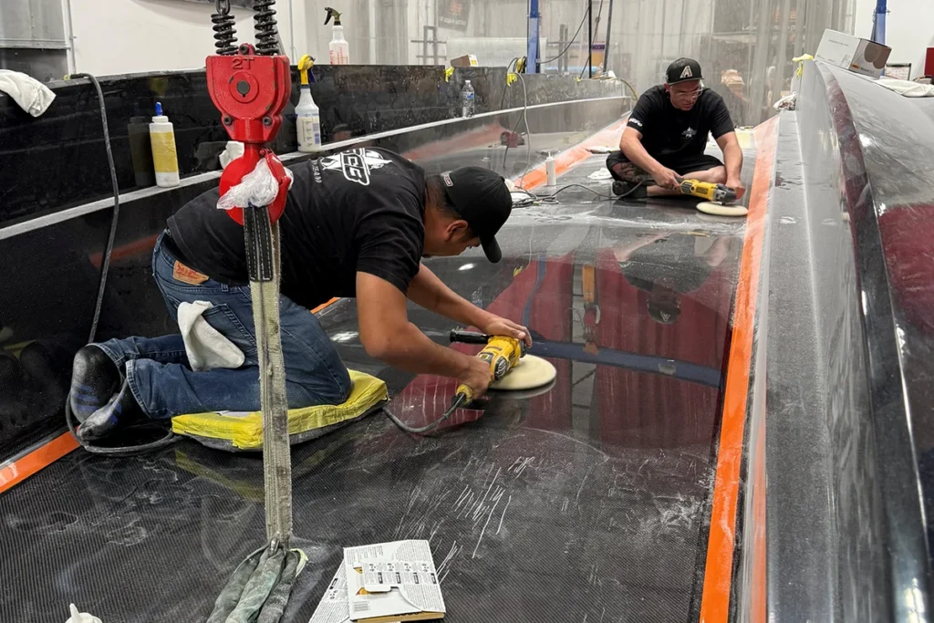 Workers performing surface finishing on a custom boat, using polishing tools and sanding techniques to achieve a high-gloss gelcoat surface, emphasizing DCB Performance Marine's meticulous craftsmanship.